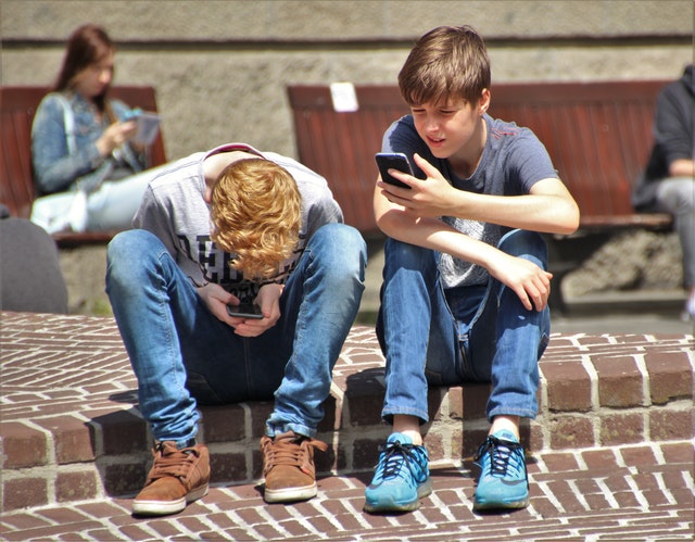 2-boy-sitting-on-brown-floor-while-using-their-smartphone
